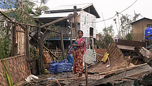 Eine Frau steht in Myanmar in den Trümmern ihres Hauses.