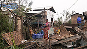 Eine Frau steht in Myanmar in den Trümmern ihres Hauses.