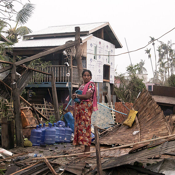 Eine Frau steht in Myanmar in den Trümmern ihres Hauses.