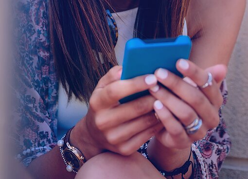 Eine Teenagerin hält ihr Mobiltelefon mit beiden Händen .