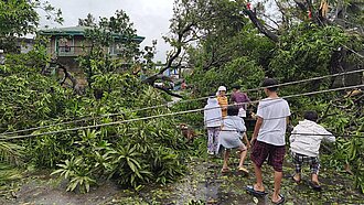 Kinder bahnen sich einen Weg durch umgestürzte Strommasten und abgerissene Äste