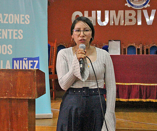 Eine Frau steht auf einer Bühne und spricht in ein Mikrofon