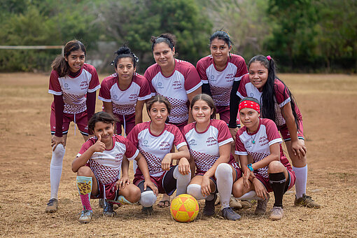 Eine Gruppe Mädchen und junger Frauen in einheitlichen Fußballtrikots stehen und knien für ein Gruppenbild beisammen.
