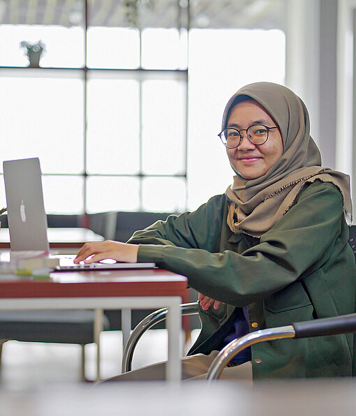 Qonita ist Absolventin des „Work in Tech“-Programms für IT-Jobs Eine Frau sitzt am Laptop