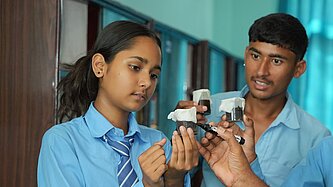 Ein Mädchen und ein Junge aus Nepal, beide in Schuluniform, analysieren eine Flüssigkeit in einem Messbecher