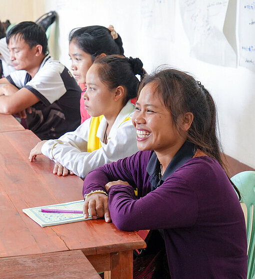 Singh sitzt lachend zusammen mit anderen Frauen und Männern an einem langen Tisch und lernt die Vorteile der Reisbanken kennen 