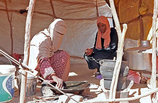 Weam (re.) und ihre Mutter bereiten in ihrer Notunterkunft eine Mahlzeit zu Zwei Frauen in einer Strohhütte