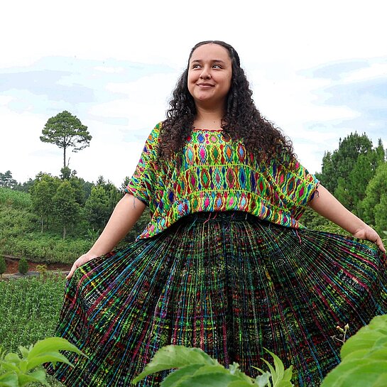 Jaqueline steht in der Mitte einer grünen Wiese und blickt selbstbewusst in die Kamera.