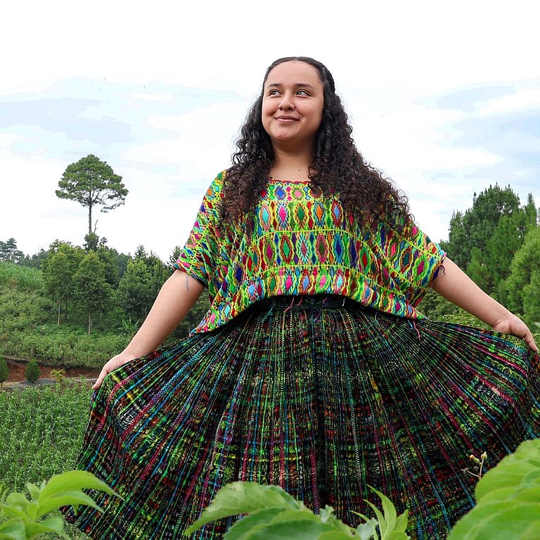Jaqueline steht in der Mitte einer grünen Wiese und blickt selbstbewusst in die Kamera.