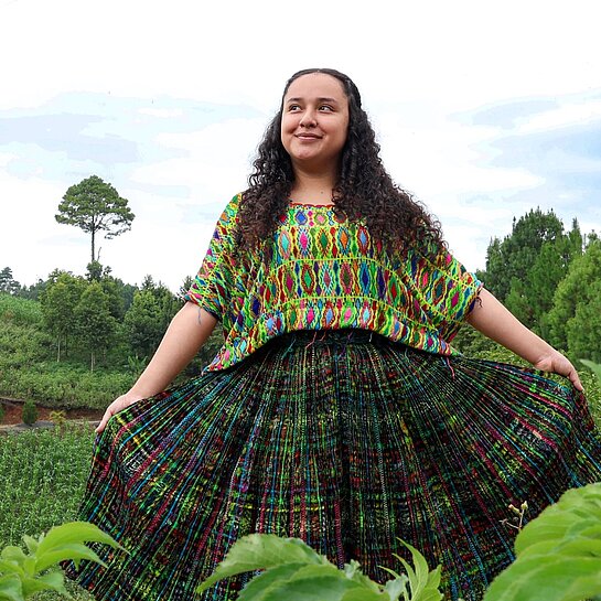 Jaqueline steht in der Mitte einer grünen Wiese und blickt selbstbewusst in die Kamera.