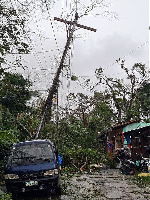 Durch die Schäden sind viele Familien vollkommen von der Außenwelt abgeschnitten Ein Haus und ein Auto stehen unter einem schief hängenden Strommast