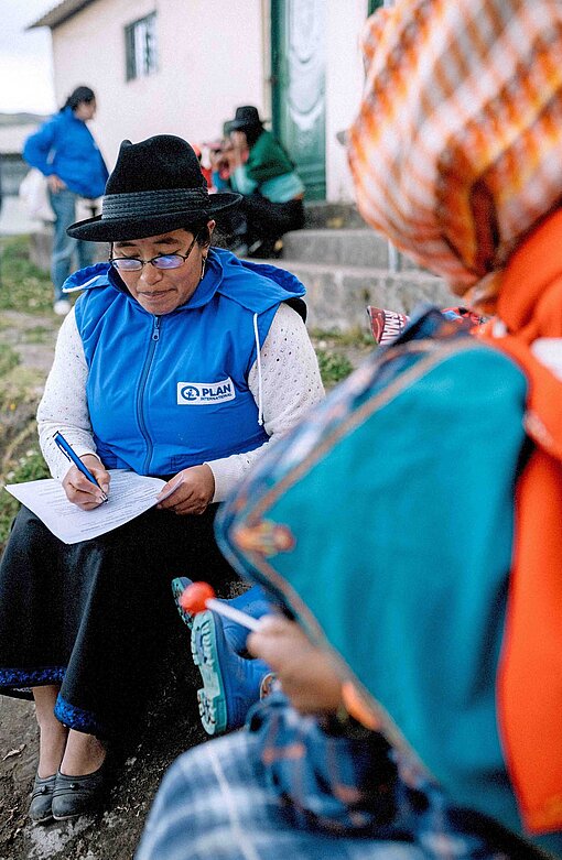 Eine Frau mit Plan-Logo an der Bekleidung notiert Rückmeldungen aus einer Befragung von Kindern