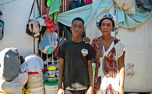 Junior (16) ist mit seiner Familie vor der eskalierenden Gewalt aus der Hauptstadt Port-au-Prince in eine Notunterkunft geflohen Ein Junge steht mit einer Frau vor einem Haus