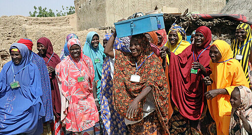 In Maradi, Niger, sprechen sich die Frauen einer Spargruppe klar gegen Kinderheirat und für die Bildung von Mädchen aus Frauen in bunten Gewändern stehen lachend auf einem Platz