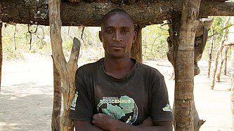 Ein Mann steht unter einer Holzhütte und hat die Arme vor der Brust verschränkt