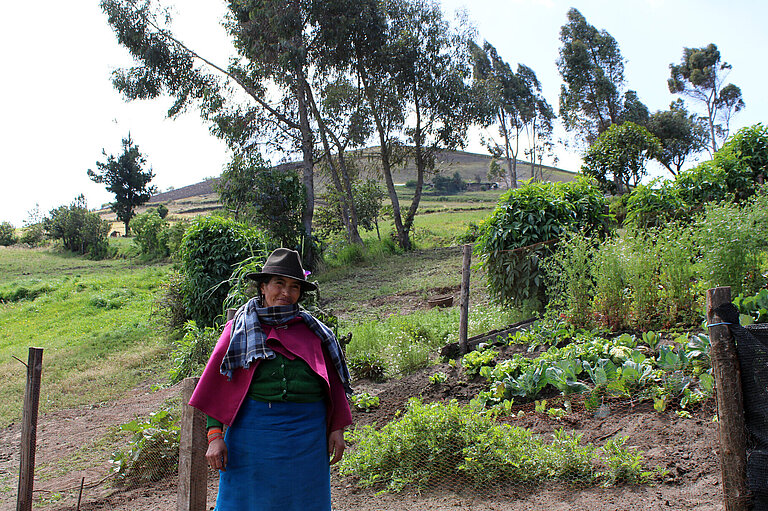 Indigene Ecuadorianerin vor einem Gemüsegarten
