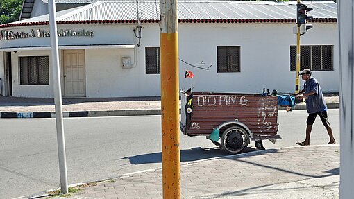 In Dili leben einige vom Dosen- und Flaschen-Recycling. Mann schiebt Karre auf Rädern durch die STraße.