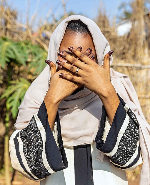 Eine junge Frau verdeckt mit ihren Händen das Gesicht