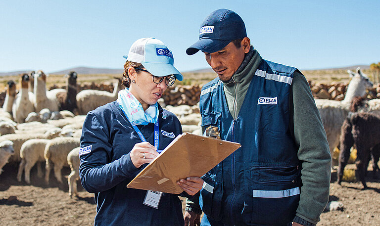 Eine Frau und ein Mann mit dem Logo vomn Plan International auf ihrer Bekleidung beraten sich über eine Liste gebeugt