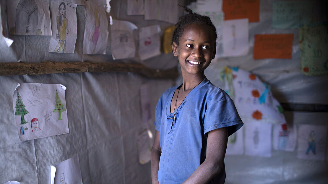 Ein Mädchen steht seitlich zur Kamera. Sie schaut über ihre Schulter und Lacht.