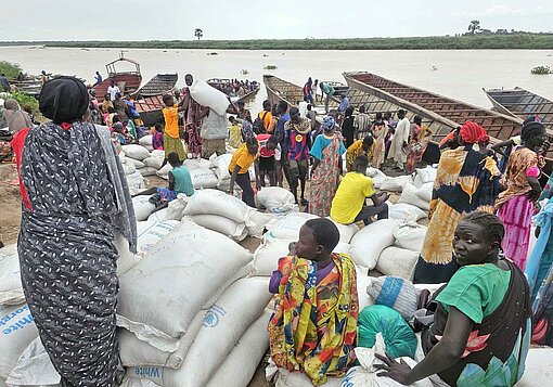Da es in Südsudan an Straßen fehlt, sind die Menschen wie hier im Bundesstaat Oberer Nil oftmals auf Boote angewiesen Am Ufer eines Flusses liegen mehrere Booto aus Metall und Menschen transportieren Güter zu den Booten