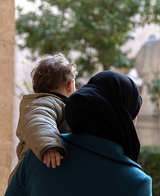 Eine Frau hält ein kleines Kind im Arm, sie sind von hinten fotografiert