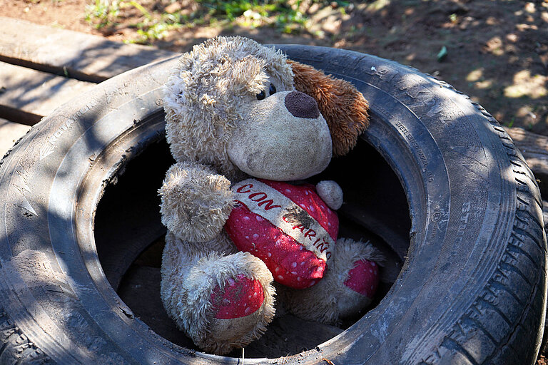 Ein abgenutzter Teddybär mit einem Herz in den Armen liegt in einem Autoreifen