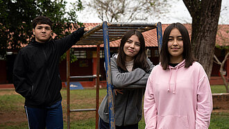 Drei Jugendliche posieren an einem Klettergerüst auf einem Spielplatz