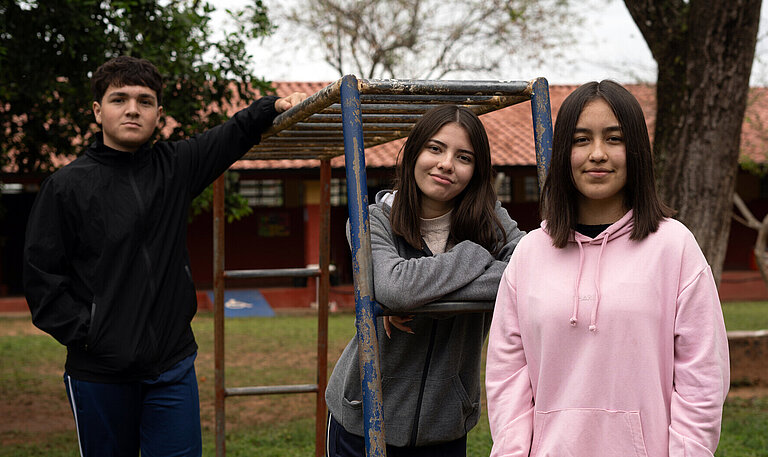 Drei Jugendliche posieren an einem Klettergerüst auf einem Spielplatz