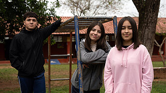 Drei Jugendliche posieren an einem Klettergerüst auf einem Spielplatz