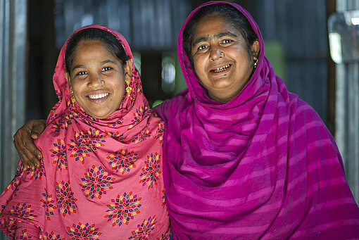 Zwei Frauen mit bunten Kopftüchern stehen nebeneinander und lachen in die Kamera
