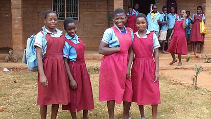 Vier Mädchen in Schuluniformen stehen nebeneinander draußen vor einem Schulgebäude