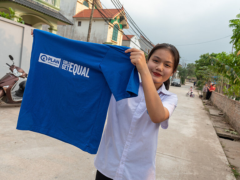 Mädchen hält blaues "Girls Get Equal" T-Shirt