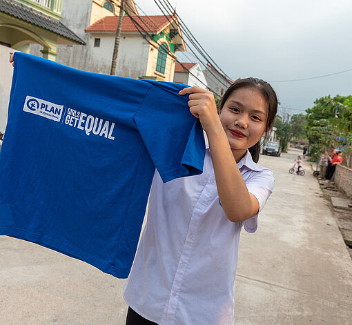 Mädchen hält blaues "Girls Get Equal" T-Shirt
