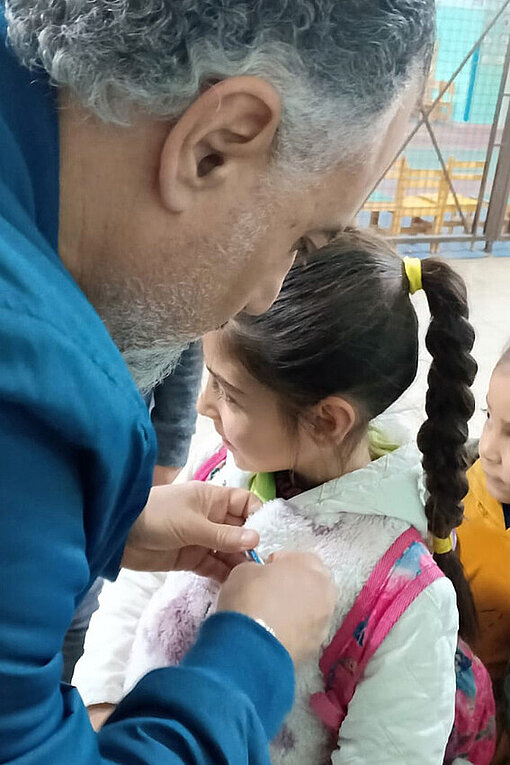 Ein Mädchen erhält ein Motivationsabzeichen von einem Plan-Mitarbeiter 