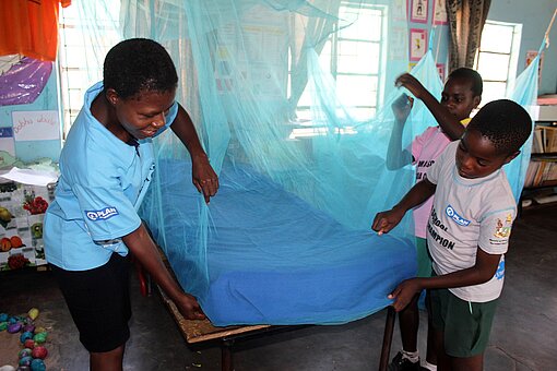 Moskitonetze schützen vor Malaria Kinder spannen ein Moskitonetz über ein Bett