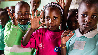 drei Kinder schauen in die Kamera und winken