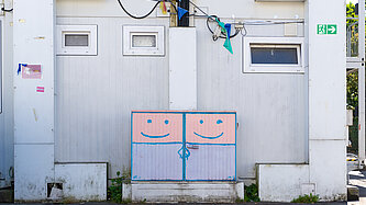 Ein Containergebäude mit einer bemalten Versorgungsbox, auf der zwei lächelnde Gesichter zu sehen sind.