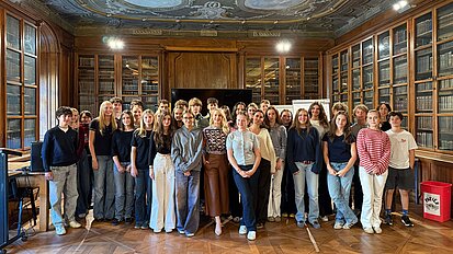 Silvia Schneider steht mit einer Schulklasse in einer Bibliothek für ein Gruppenfoto nach ihrem Vortrag.