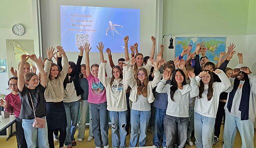Plan-Botschafterin Lisa Buchner erzählte einer Wiener Schulklasse, wie der Traum vom Fliegen für sie wahr wurde Kinder stehen in einer Klasse und jubeln mit erhobenen Händen