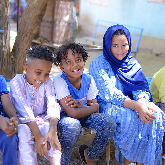 Ein Mädchen sitzt mit ihren fünf jüngern Brüdern auf einer Mauer