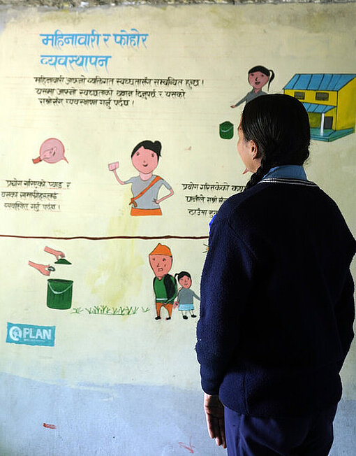 Ein spezieller Raum für Menstruationshygiene bietet Mädchen im Distrikt Kalikot während ihrer Periode Rückzug, Wärmflaschen und Erste-Hilfe-Kits Ein Mädchen steht im Ruheraum für Menstruationshygiene an einer Schule in Kalikot und schaut ein buntes Wandbild an