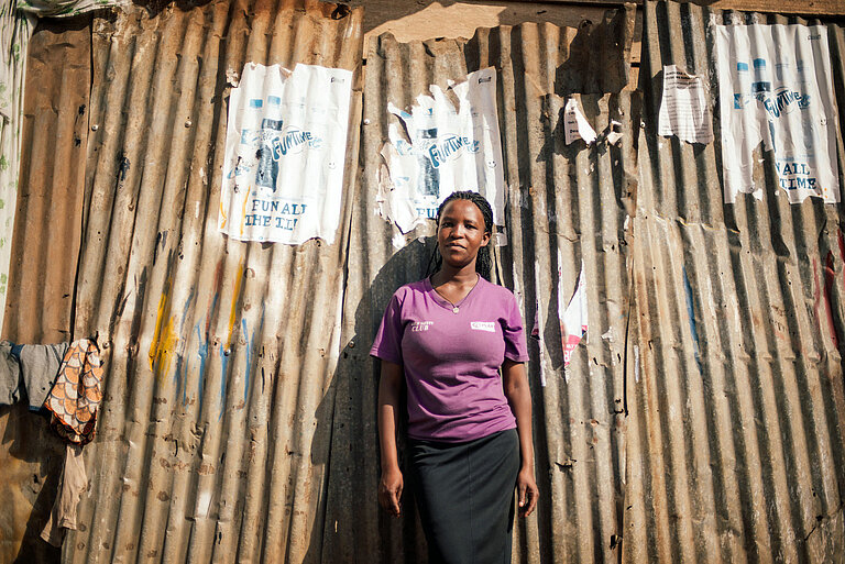 Eine Frau lehnt an der Wellblechwand eines Slums in Uganda