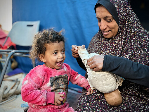 Suhad spielt mit ihrer jüngsten Tochter Eine Mutter spielt mit ihrer kleinen Tochter. Sie hält eine Puppe in der Hand