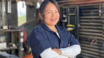 Eine junge Frau steht mit verschränkten Armen in einer Motorradwerkstatt 