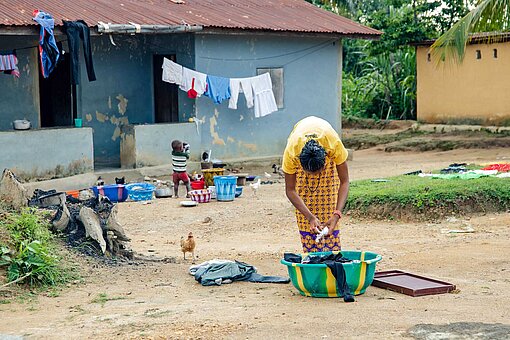Kochen, waschen, putzen und den Haushalt versorgen – in Sierra Leone liegen diese Aufgabe meistens bei den Mädchen und Frauen Eine Frau beugt sich über eine Wanne mit Wäsche