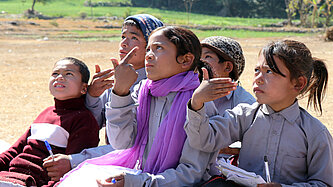 Fünf Kinder sitzen auf dem Boden und schauen nach oben. Einige von ihnen gestikulieren in Gebärdensprache
