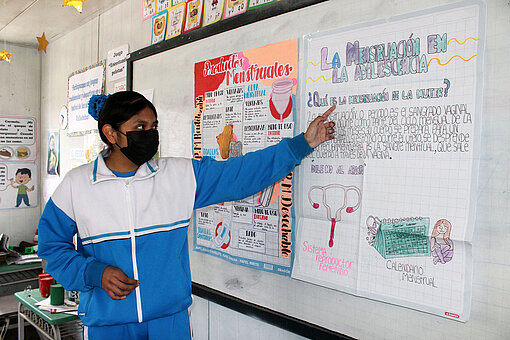 Dulce entkräftet Mythen rund um die Menstruation in ihrer Gemeinde in Peru. Eine junge Frau steht vor einem Plakat, auf dem Fakten und Bilder zum Thema Menstruation stehen.