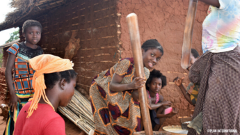 Junge Frauen bereiten Essen vor einer Lehmhütte zu.