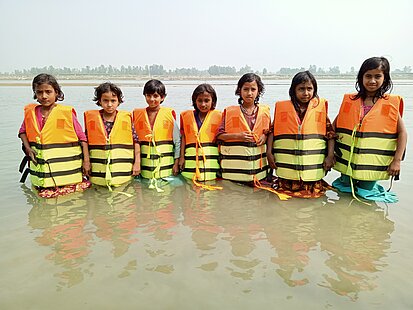 Sieben Kinder in Rettungswesten stehen bis zur Hüfte im Wasser